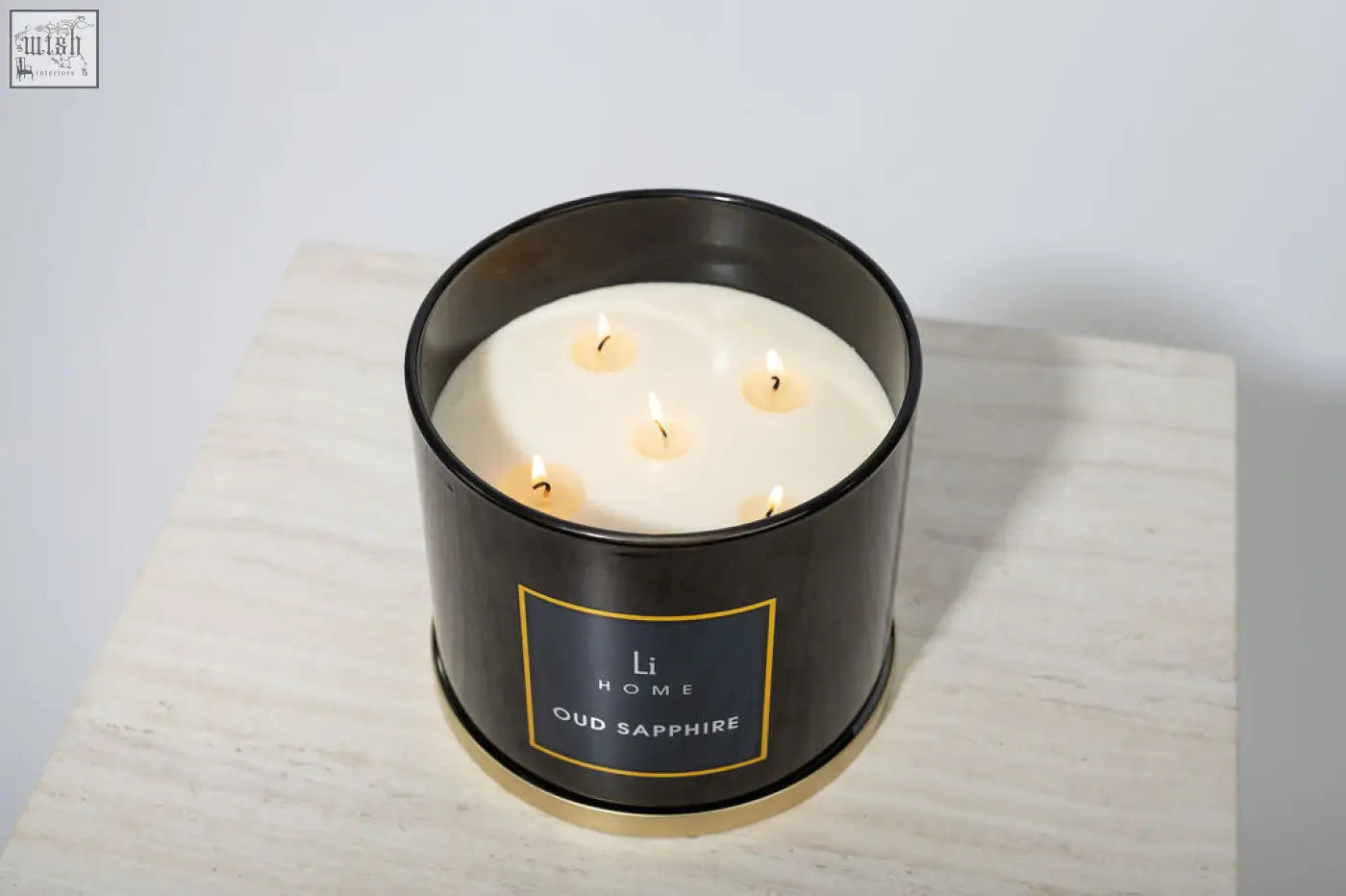 Black cylindrical large candle from li home oud sapphire collection with five lit wicks in metal container with gold trim