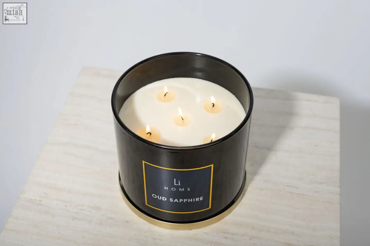 Black cylindrical large candle from li home oud sapphire collection with five lit wicks in metal container with gold trim