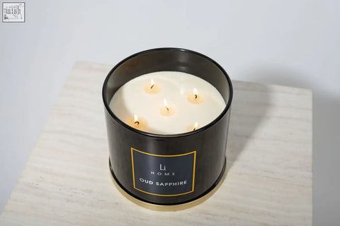 Black cylindrical large candle from li home oud sapphire collection with five lit wicks in metal container with gold trim