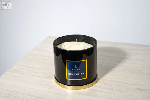 Black cylindrical large candle jar with gold trim and blue li home oud sapphire label containing three white wicks