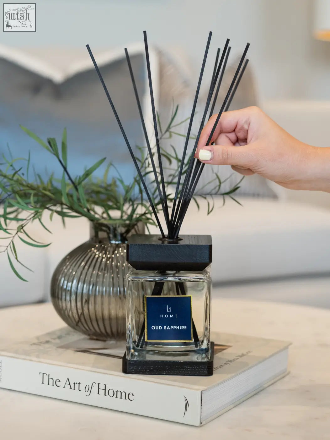 Black reed diffuser with clear glass square bottle and dark wooden base labeled li home oud sapphire lifestyle home scent