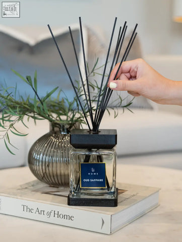 Black reed diffuser with clear glass square bottle and dark wooden base labeled li home oud sapphire lifestyle home scent