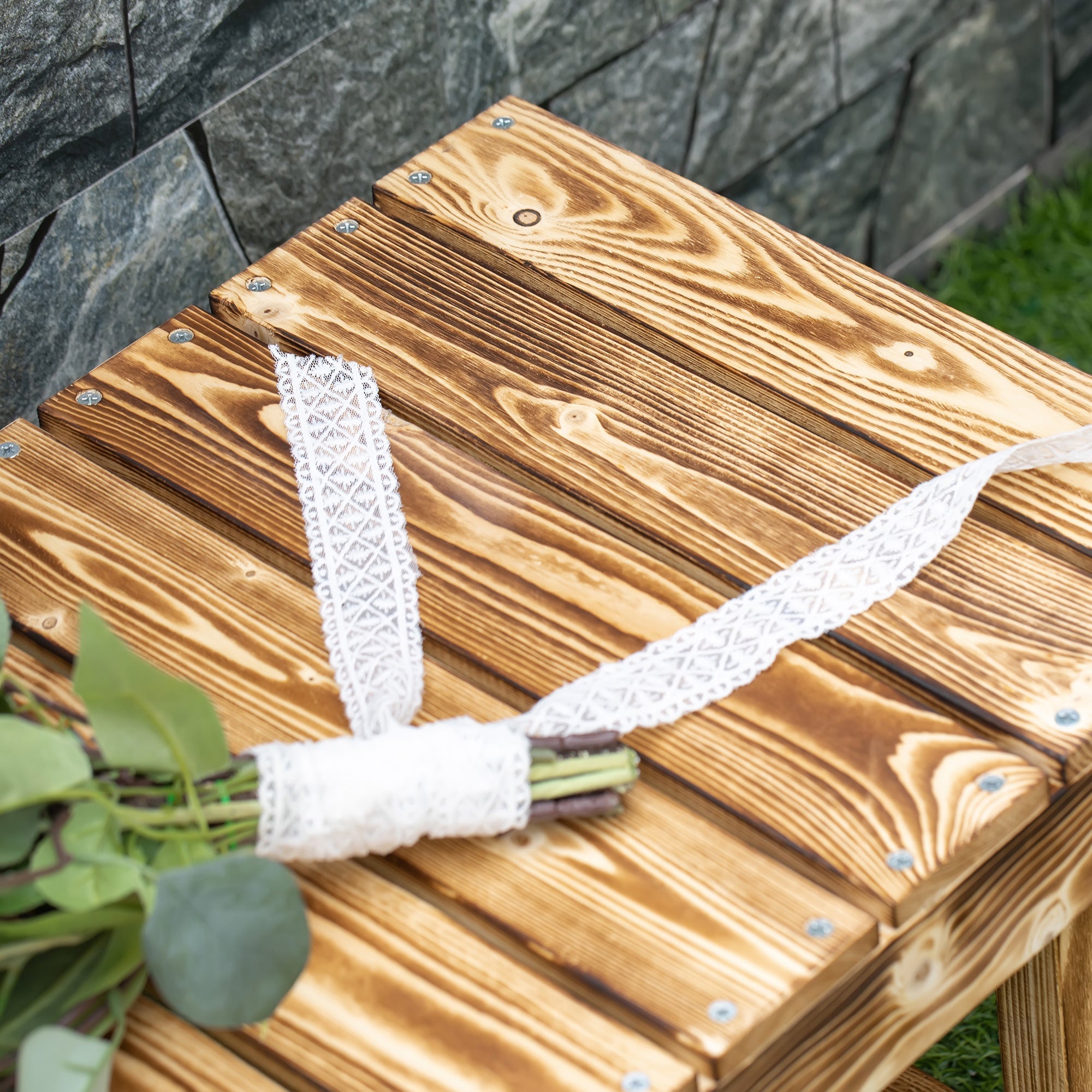 White lace ribbon wrapped around greenery on a solid fir wood 110l x 38w carbonised fir wood garden bench