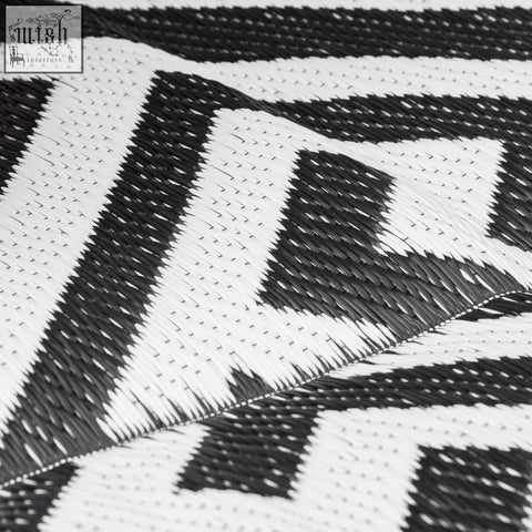 Black and white woven outdoor rug with geometric zigzag pattern made of plastic straw perfect for road tour use