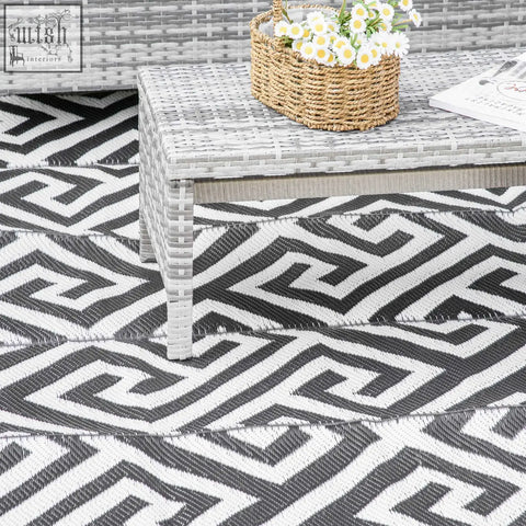 Gray woven wicker coffee table with daisies on top next to black and white reversible outdoor plastic straw rug for road tour