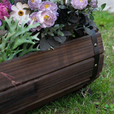 Dark brown solid wood planter with black leather strap and brass rivets filled with purple white flowers in carbonized colour