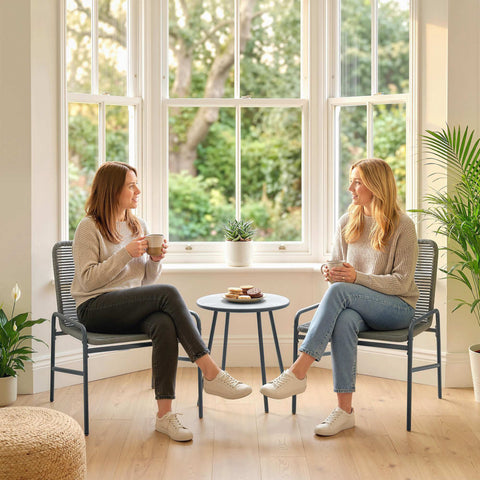 Two women sit in comfortable dark grey rattan chairs from the outsunny bistro set near a large window