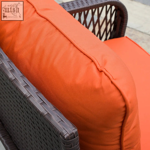 Bright orange cushion with textured fabric on dark brown wicker chair in outsunny rattan bistro set with tempered glass coffee table holding place