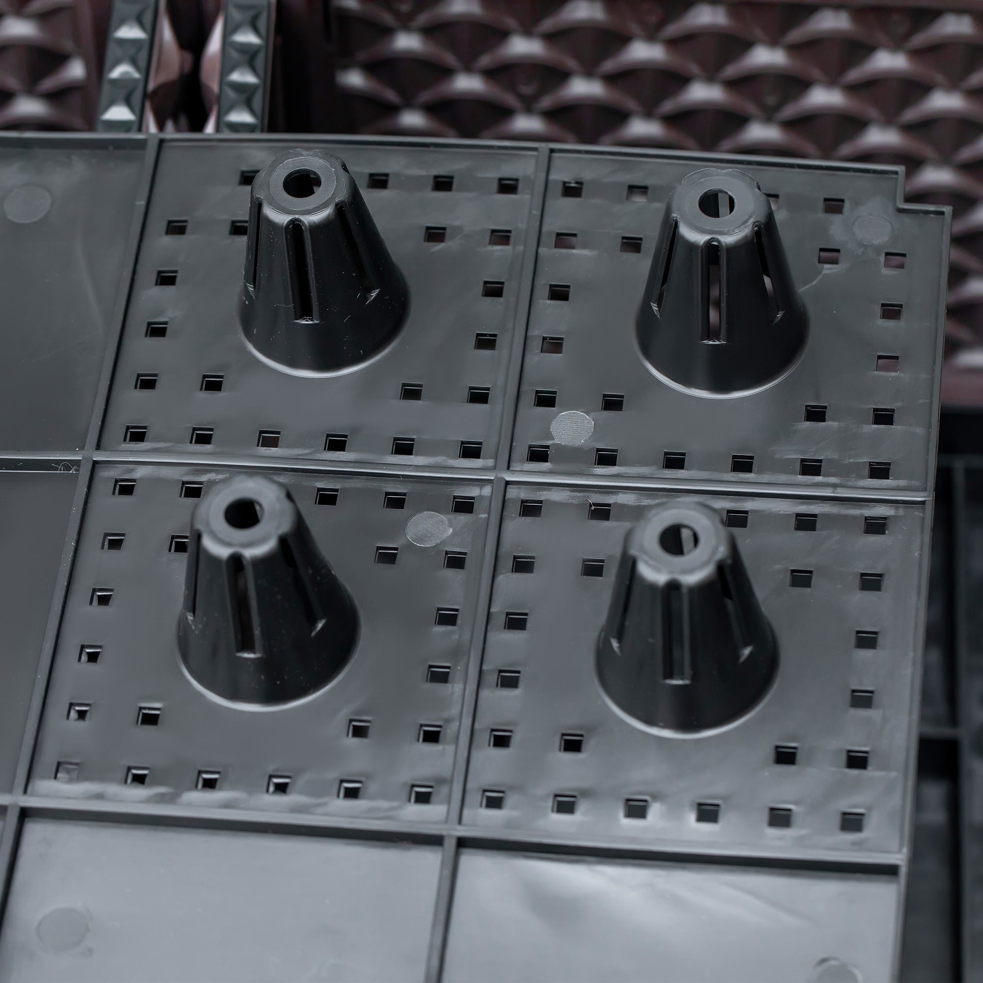 Black plastic cone-shaped connectors with drainage holes on a gray metal grid in an outsunny planter box to grow plants