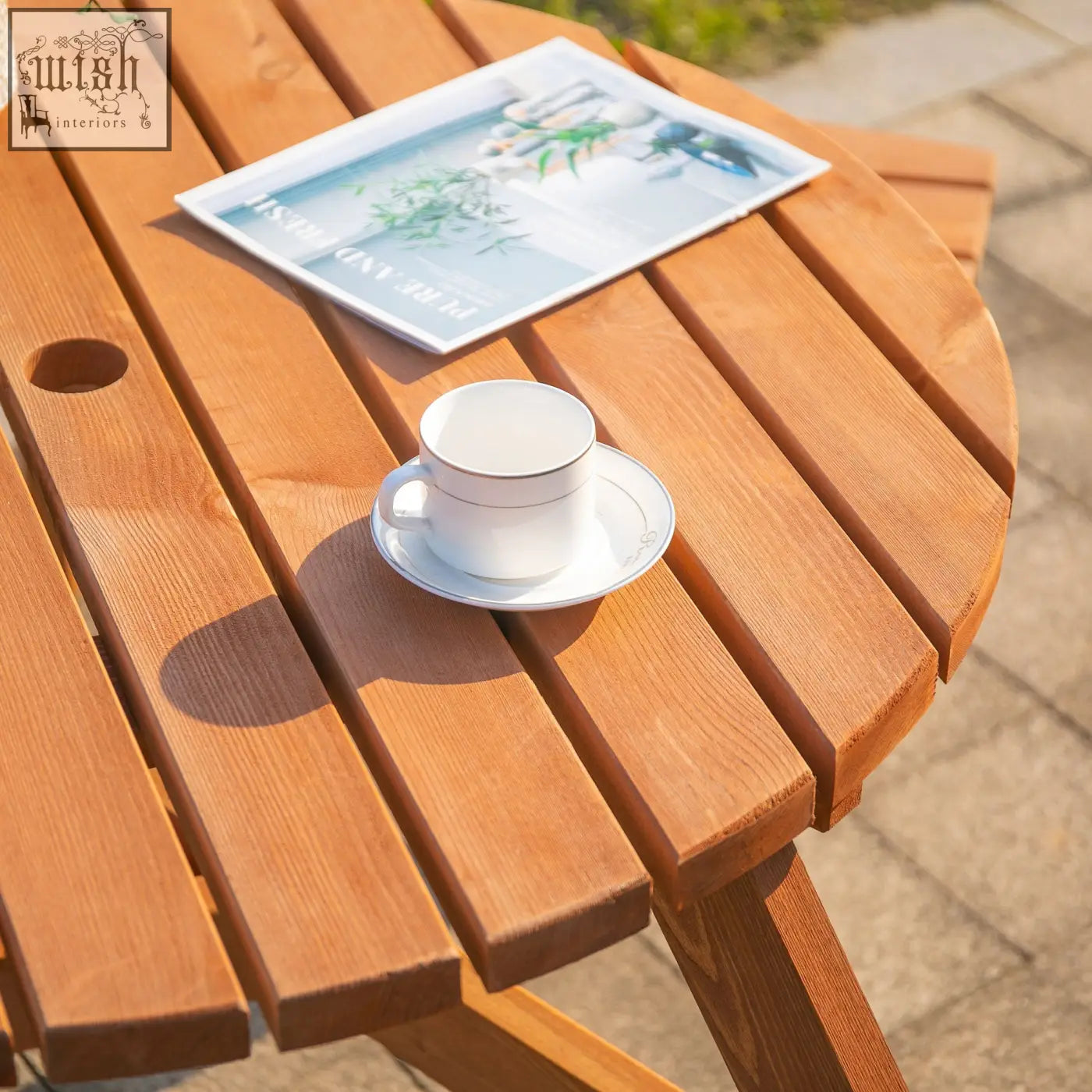 White ceramic coffee cup with gold rim on matching saucer next to brownish red fir wood construction picnic table set
