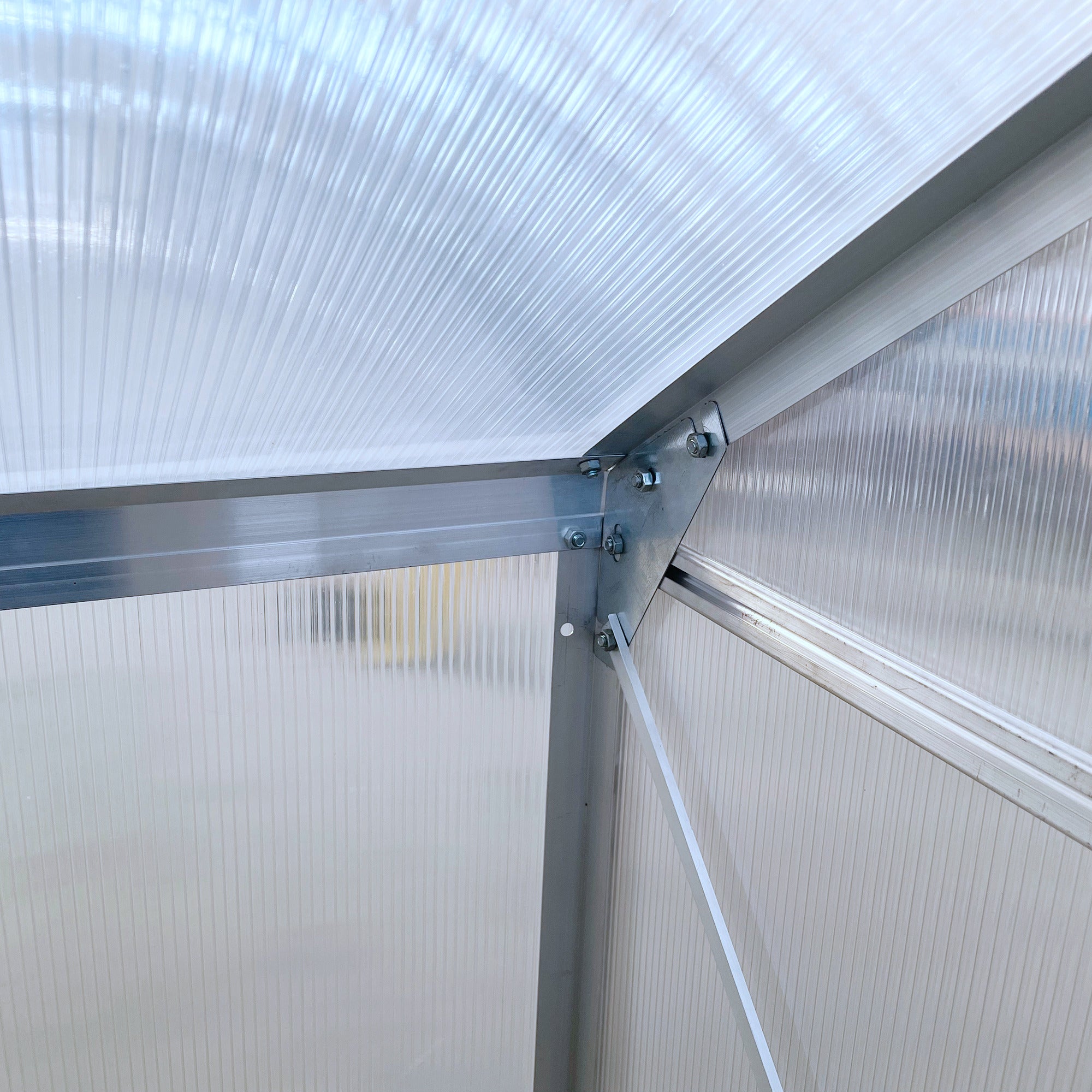 Silver aluminium alloy frame with ribbed translucent polycarbonate panels forming a lean to wall greenhouse corner
