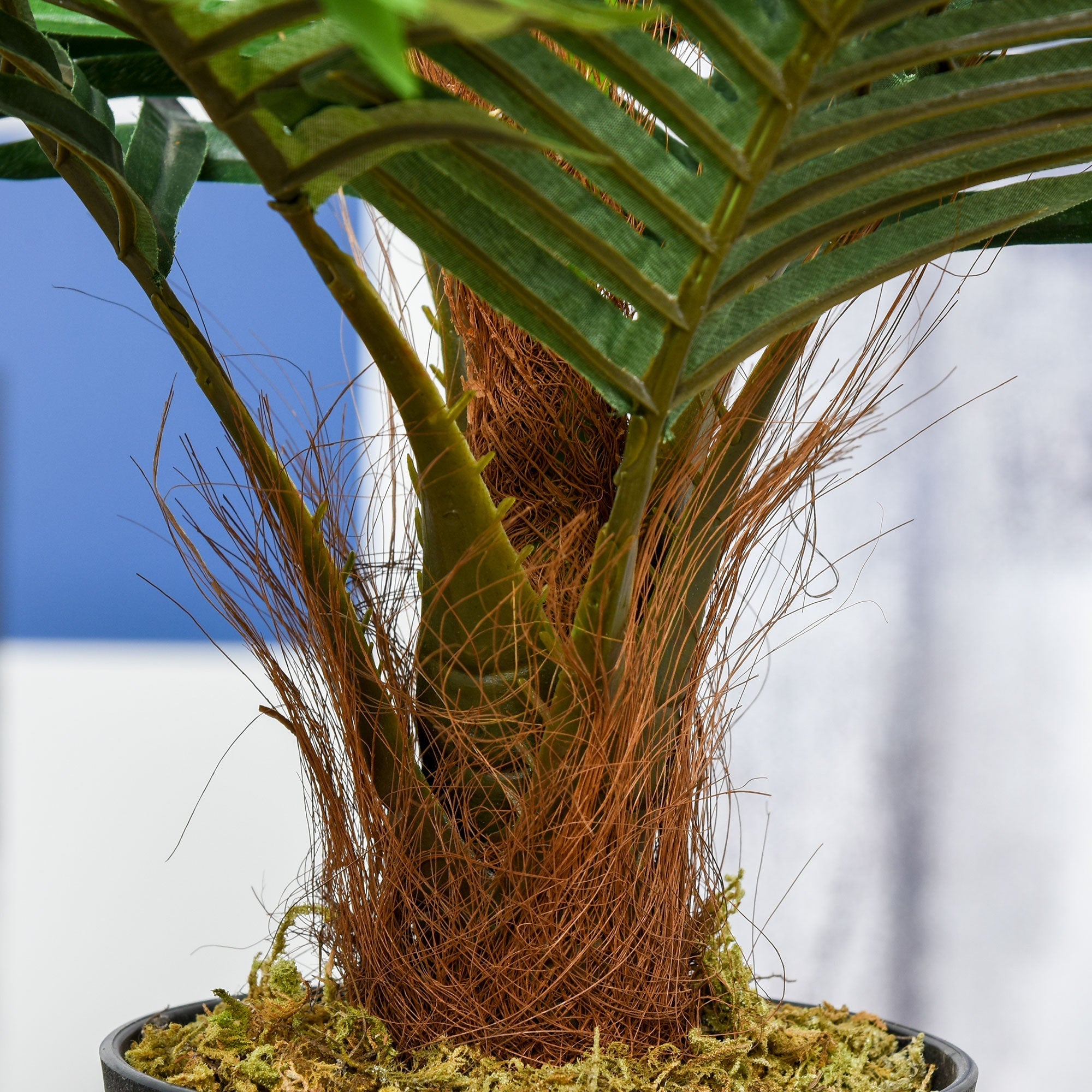 A lush green artificial palm plant with long fronds and a textured brown base in a cement-filled black pot for decor