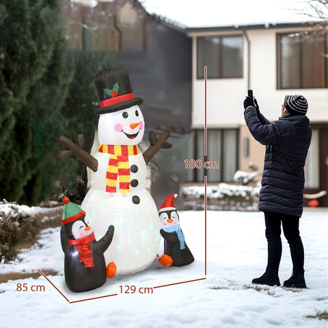 A white inflatable snowman with led lights and ground stakes stands with two penguins in a snowy yard
