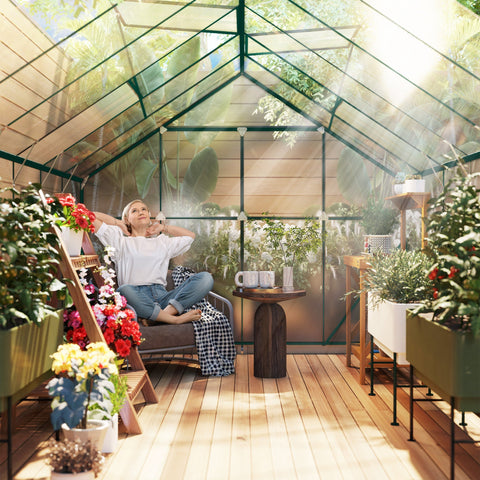 A woman sits inside a clear outsunny 8 x 12ft aluminium greenhouse with polycarbonate panels and double sliding door