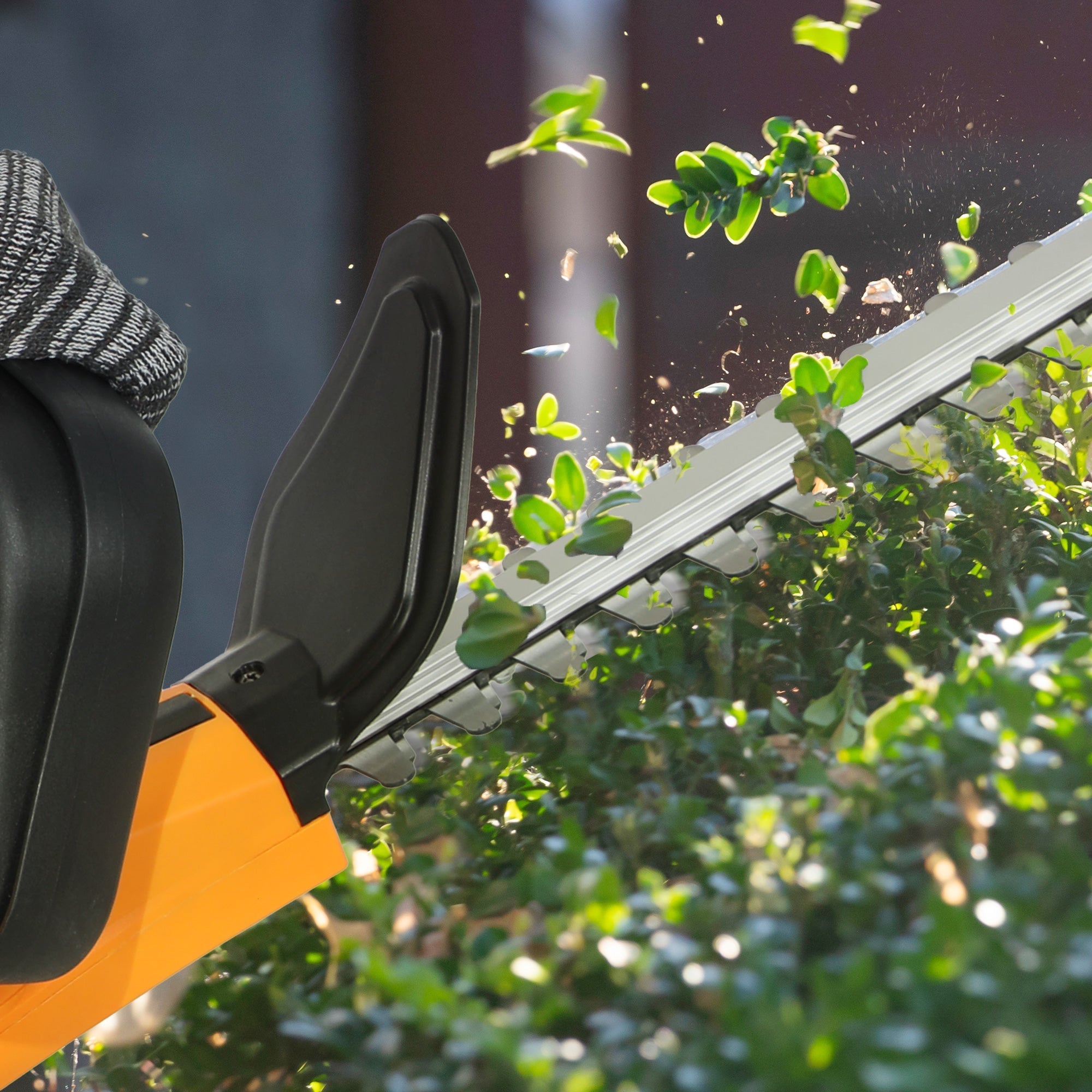 Orange and black cordless hedge trimmer cutting green foliage with sharp 51cm blade and circuit protection by Outsunny