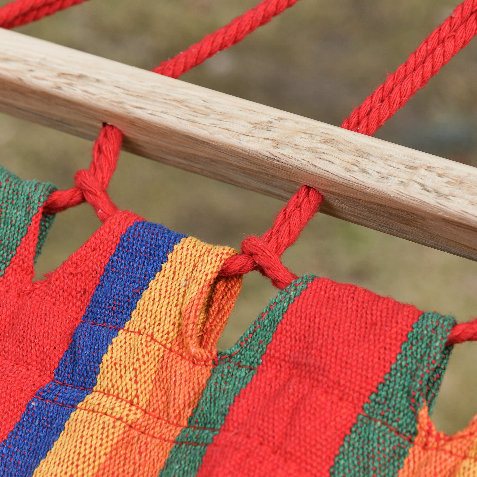 A vibrant multicolored cotton hammock with bold red blue orange and green stripes and thick red ropes perfect for indoor outdoor use