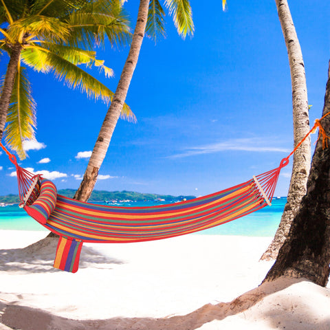 A vibrant striped outsunny cotton hammock with headrest and side pocket hangs between palm trees on a sunny beach