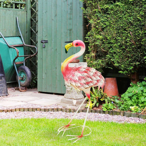 Vibrant pink and yellow metal flamingo garden statue with u-shaped ground stakes on stone pedestal for outdoor decor