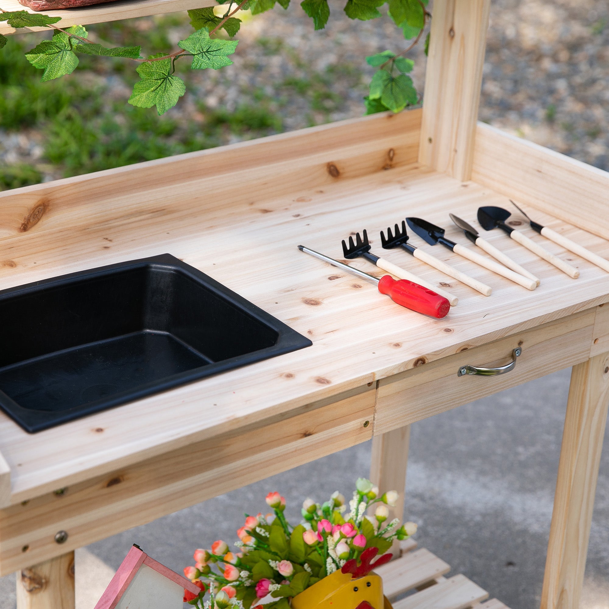 Light-colored wooden garden potting bench with black plastic sink and tools on surface for outdoor planting use