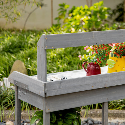 Gray wooden garden potting table with galvanized metal top, hooks, drawer, and red watering can beside flower pot