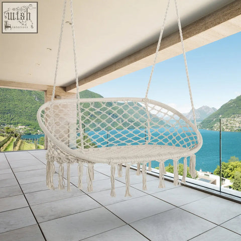 Cream-colored hanging hammock chair with woven macrame cotton rope and tassels on a sturdy metal frame for indoor and outdoor use