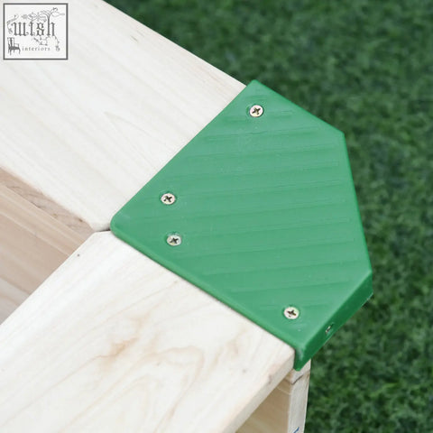 Green plastic corner protector with ribbed texture fixed by silver screws on fir wood wooden sand pit beams