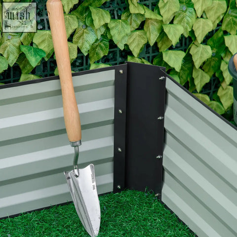 A stainless steel garden trowel with wooden handle leaning on a grey outsunny metal raised garden bed planter box