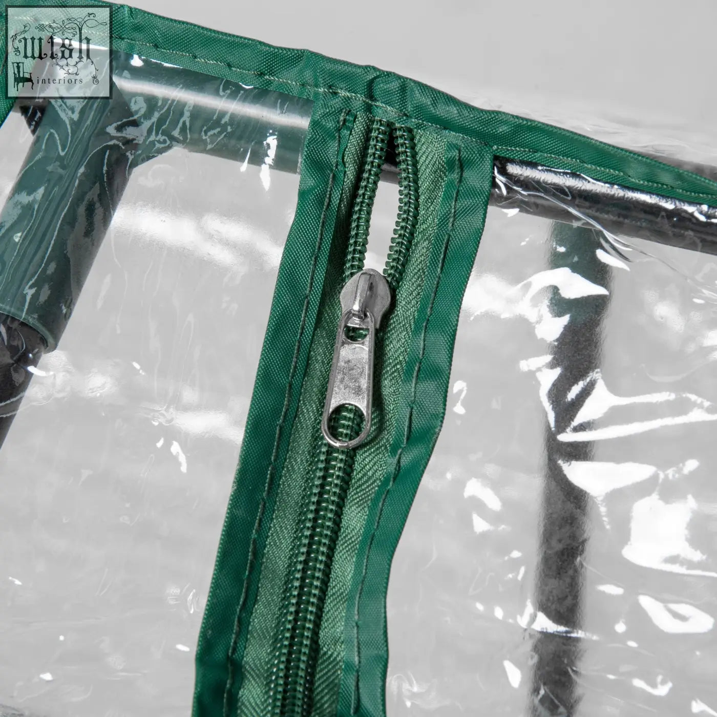 Green fabric zipper with metallic pull tab on mini greenhouse plastic cover for backyard garden planter with zipped windows