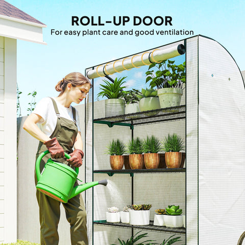Person in gardening overalls holding green plastic watering can next to outsunny mini greenhouse with steel frame and roll-up door