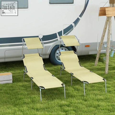 Two beige fabric reclining sun lounger chairs with metal frames and sunshades on grass in front of an rv