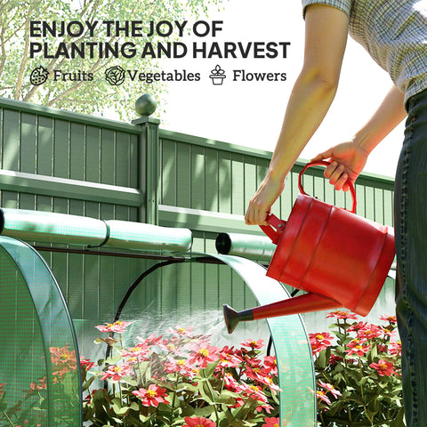 Red plastic watering can with handle and spout in front of an easy access green steel frame tunnel greenhouse