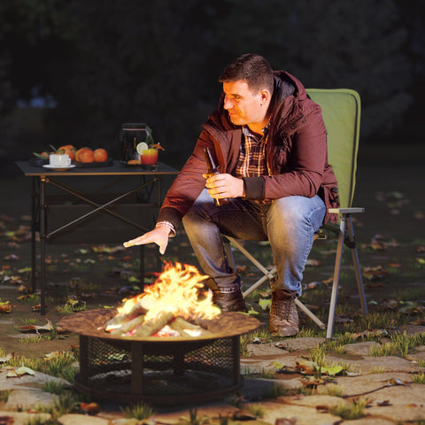 A black metal fire pit with mesh base sitting next to a green outsunny portable camping chair with padded seat and oxford cloth