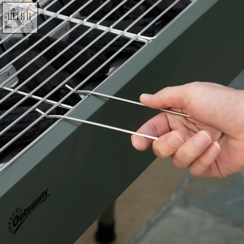 A hand holding a silver metal skewer near the charcoal grate of an outsunny portable stainless steel grill with airflow vents
