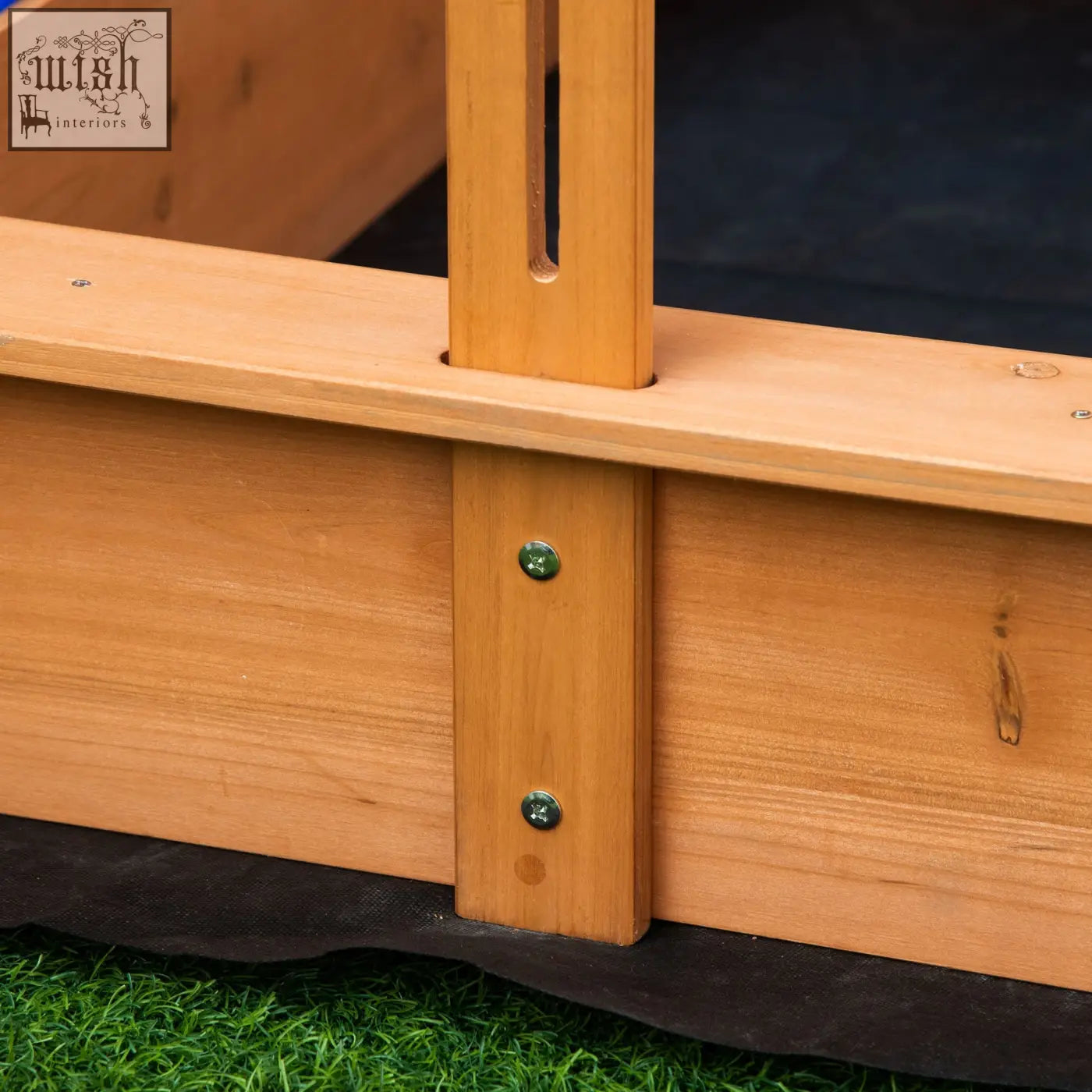 Light brown kids wooden sandbox frame with vertical slats and green screws supporting plastic basins bottomless design