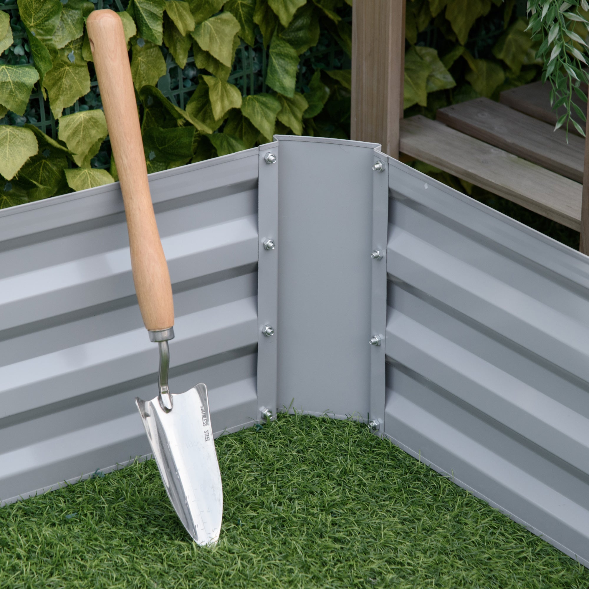 Gray corrugated metal raised garden bed with wooden handled trowel resting against outsunny planter box