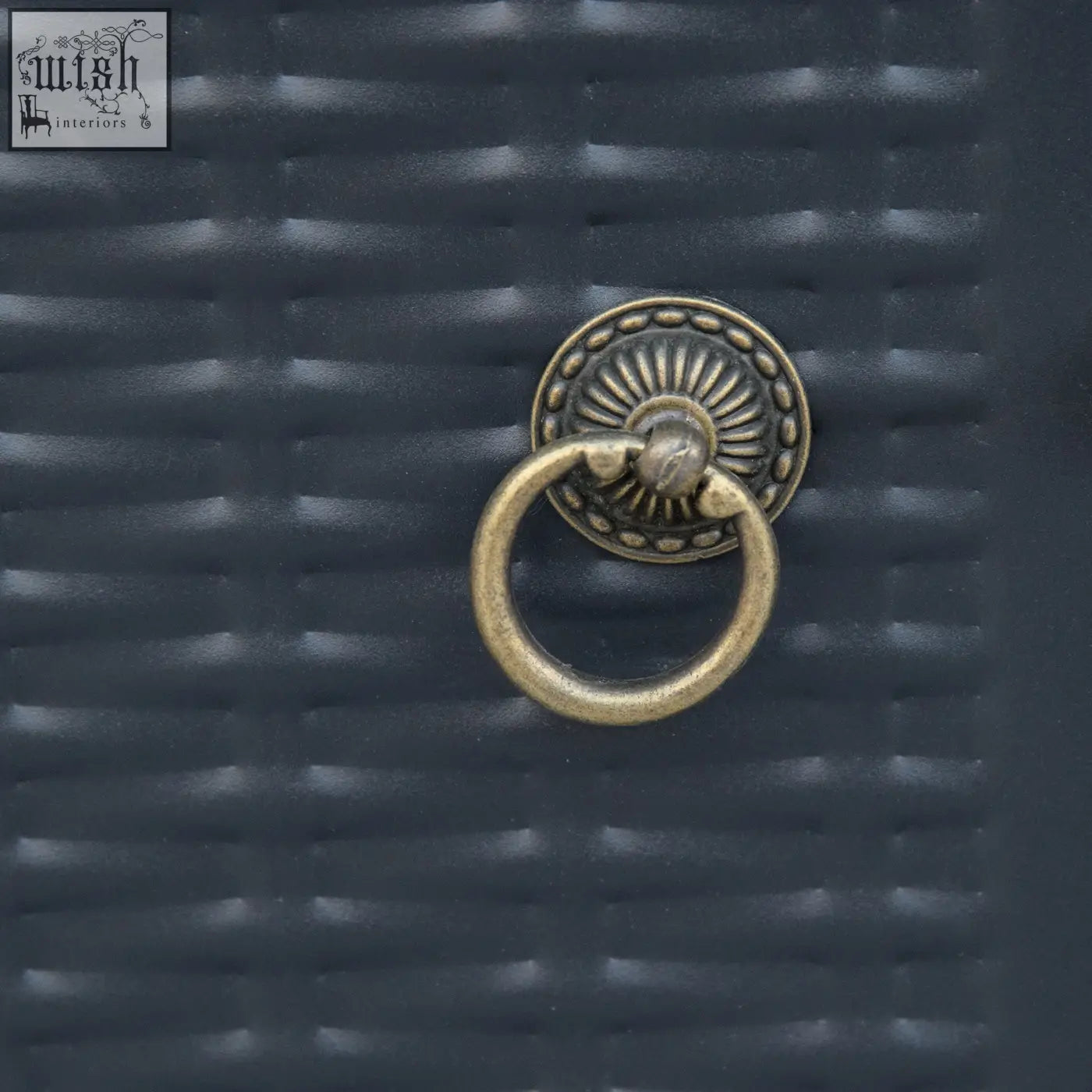 Antique brass ring pull with sunburst design on dark woven surface of black outsunny propane gas fire pit table with lava rocks