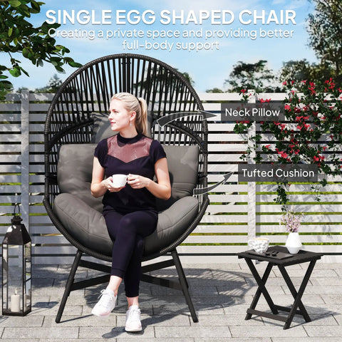 Black wicker rattan egg chair with plush gray tufted cushion and neck pillow on powder-coated steel frame outdoors