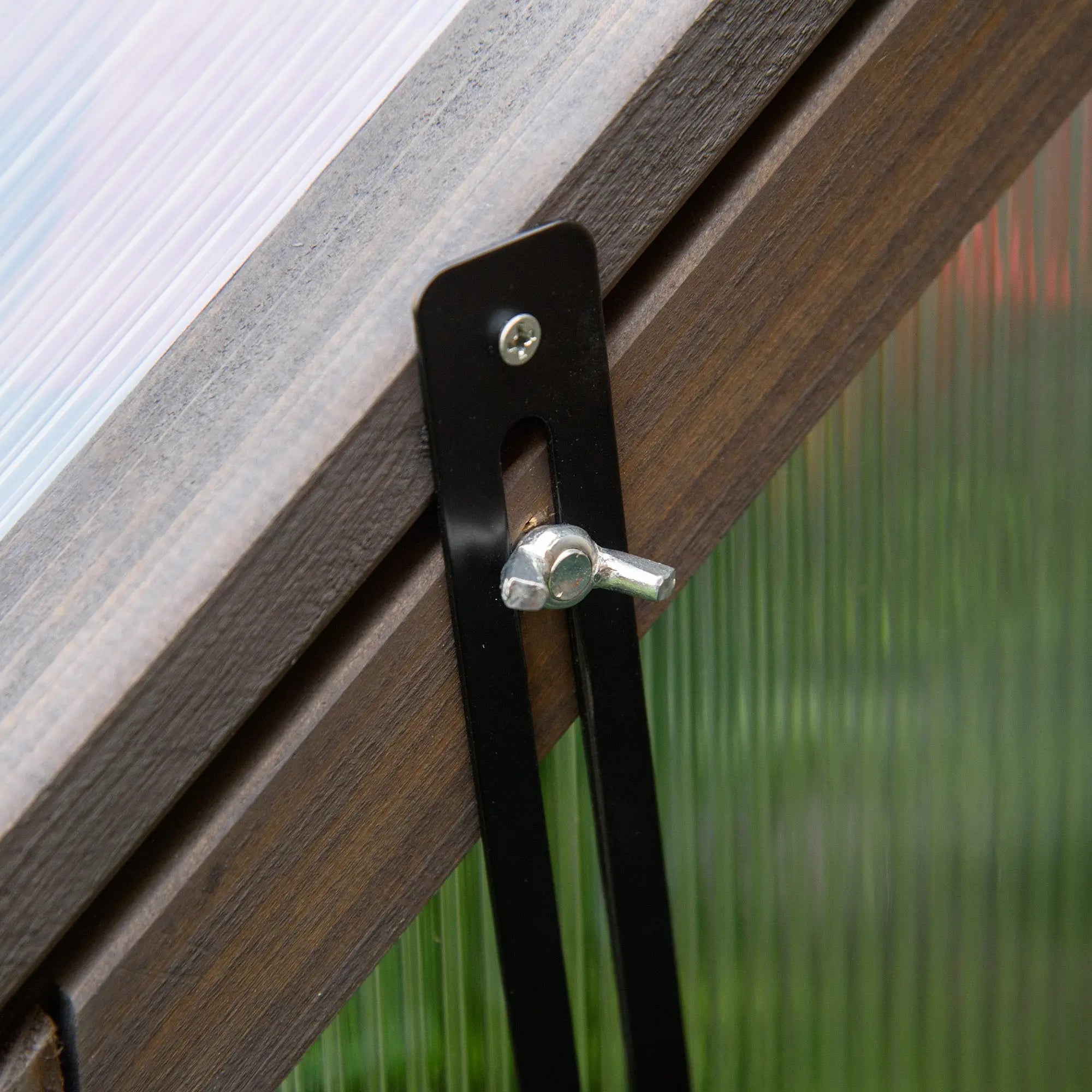 Black metal window latch with silver wing nut on dark wood siding of outsunny grey cold frame greenhouse grow house