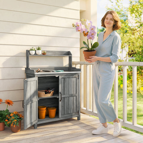 Gray wooden potting bench table with open cabinet shelves and aluminum worktop topped by white pots outdoors