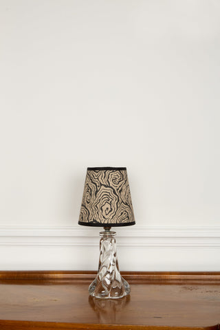 A clear glass table lamp with a faceted base and an ornate swirling beige and black oysters monochrome lampshade