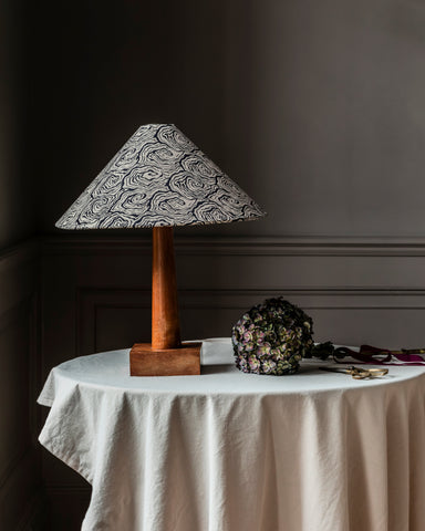 A large tapered cone lampshade with a black and white swirling pattern mounted on a polished wooden base