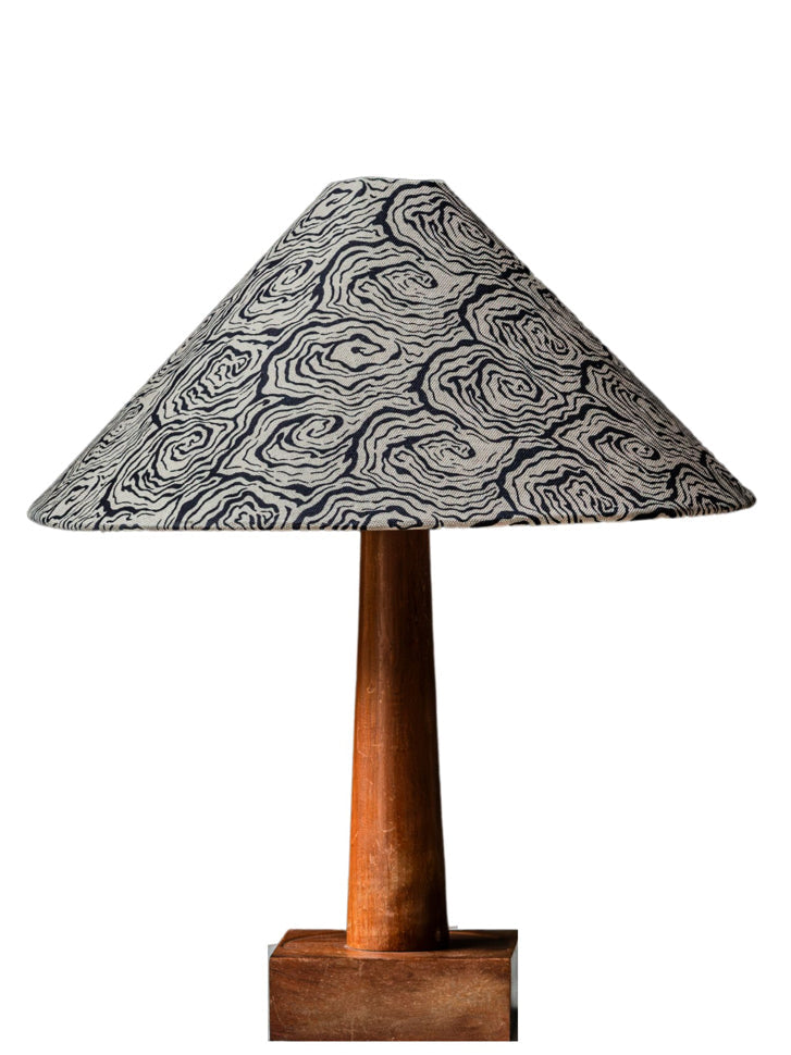 A large tapered cone lampshade with a black and white swirling pattern on a slender wooden stand