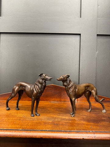 Two bronze greyhound figurines with fine details stand poised on a wooden surface as elegant dog ornaments