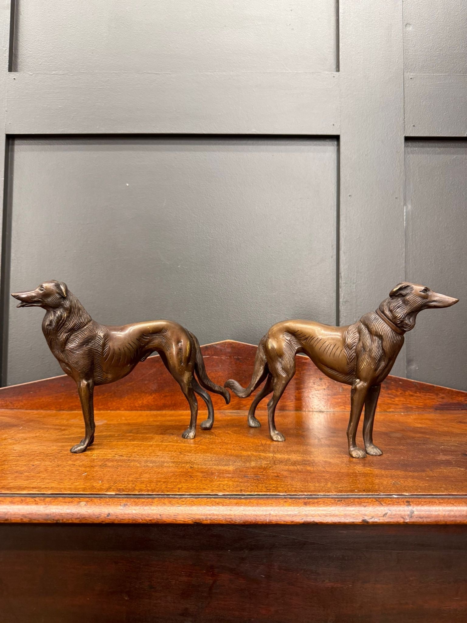Two bronze greyhound figurines with intricate details and slender builds standing side by side on a wooden surface