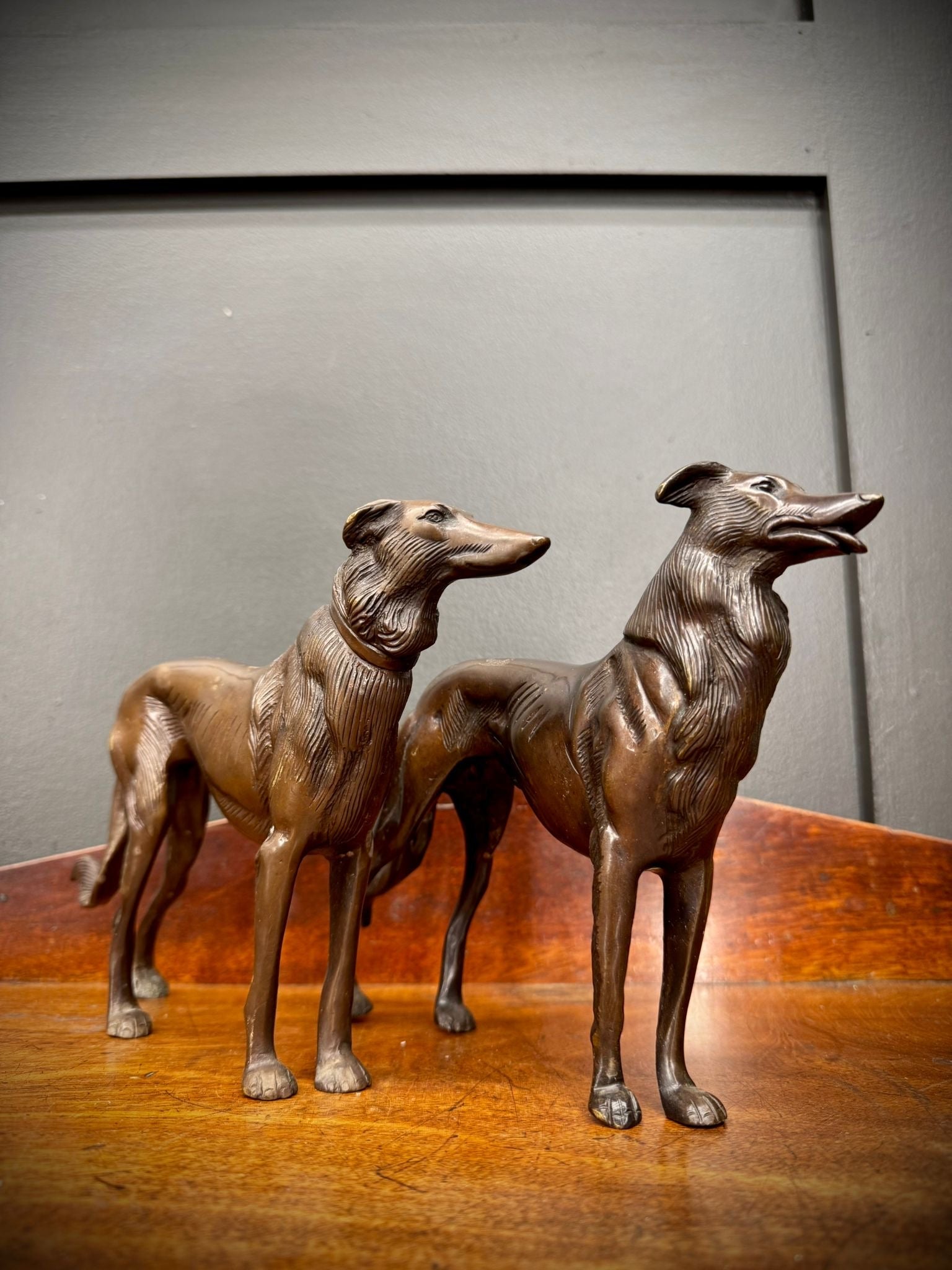 Pair of bronze greyhound figurines with intricate details and slender bodies standing side by side on a wooden surface