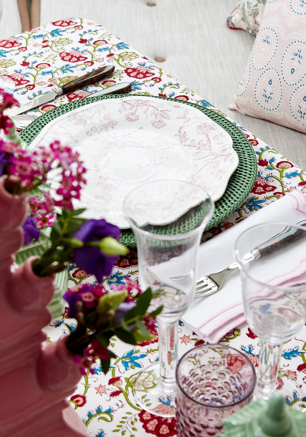 White ceramic plate with pink floral patterns on a green placemat next to a palm beach cushion cover