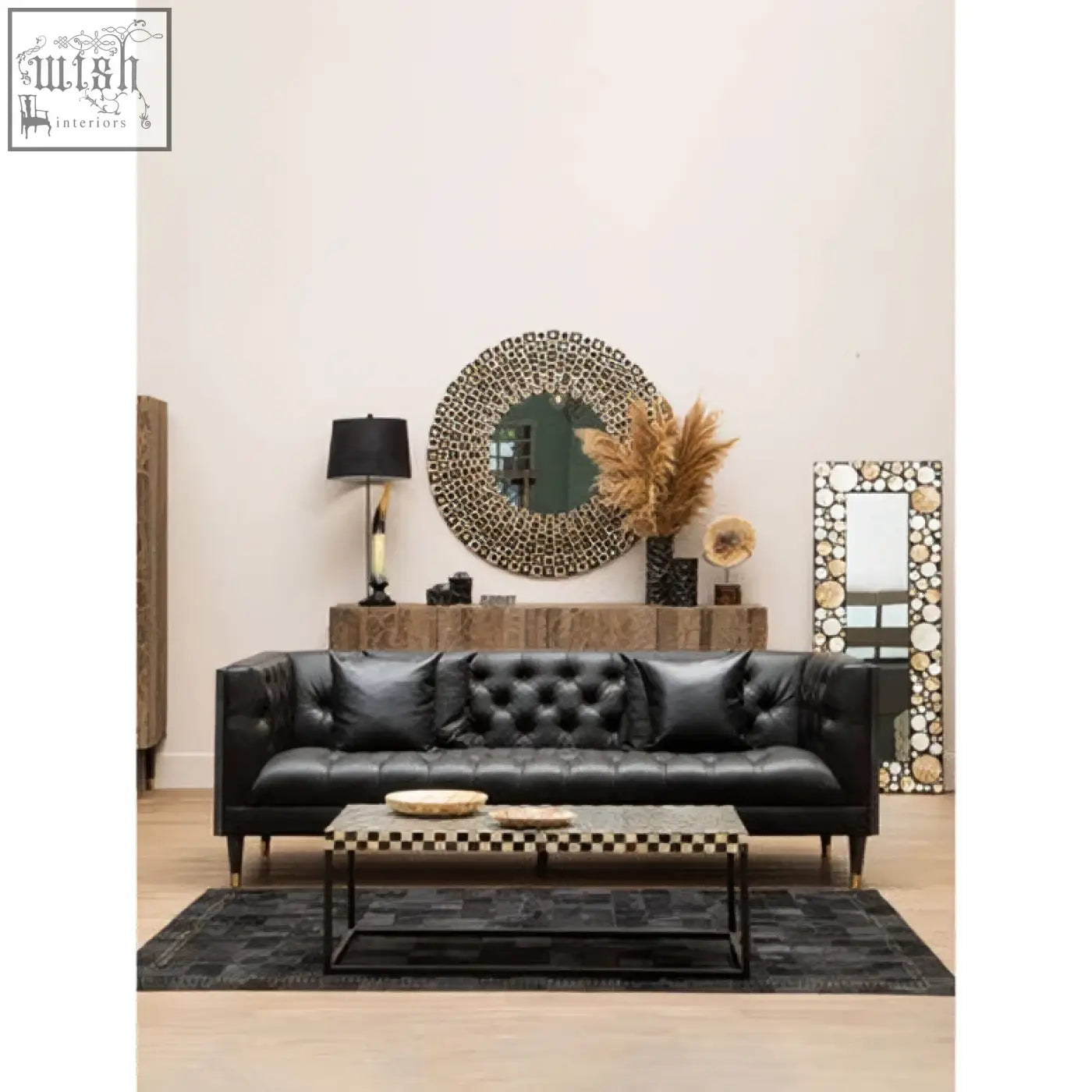 Black tufted leather sofa with dark wooden legs paired with a sleek round black wall mirror with shell inlay