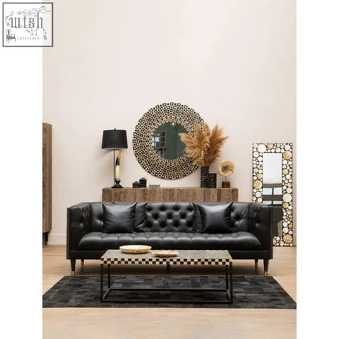 Black tufted leather sofa with dark wooden legs paired with a sleek round black wall mirror with shell inlay
