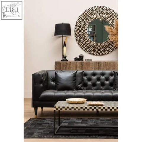 Black tufted leather sofa with sleek gold-tone legs paired with palu round black wall mirror with shell inlay