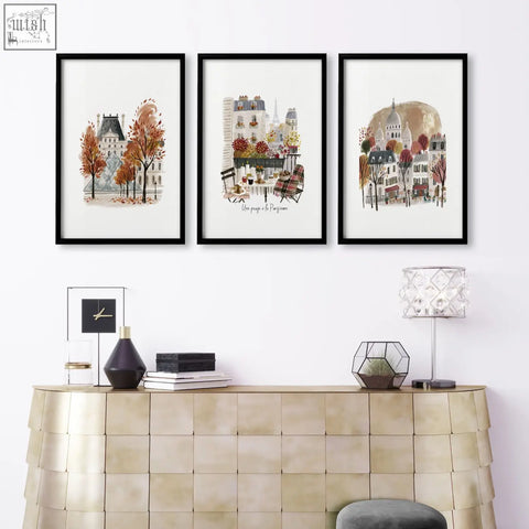Three black-framed paris travel living room wall art prints above a gold-toned console table featuring autumn scenes